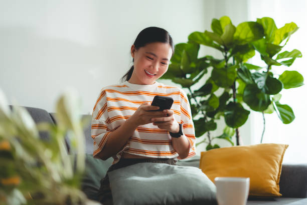 istock Asian woman happy smiling sitting on sofa and using smart phone at home. 2156275100