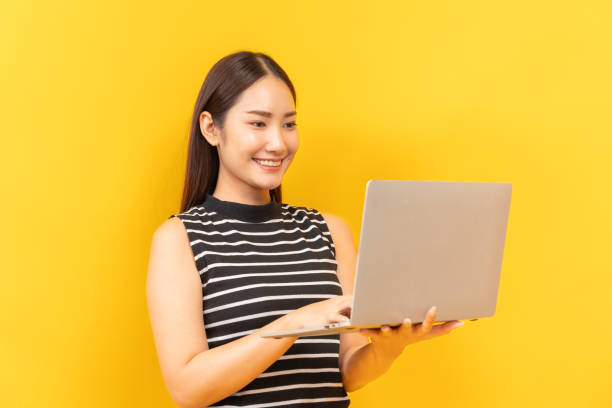 istock Young Asian woman student diligently working, holding a notebook, yellow background 2156280085