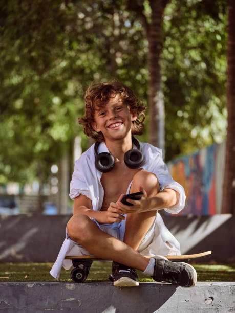 istock Cheerful boy sitting on skateboard and smiling at camera with sm 2156284248