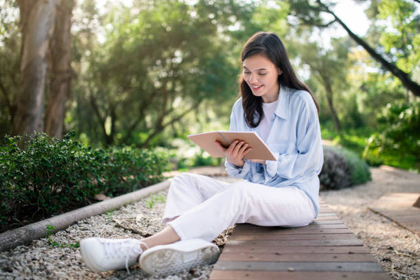 istock Engaged young woman reading from her notebook while sitting cross-legged on a wooden walkway 2156284371
