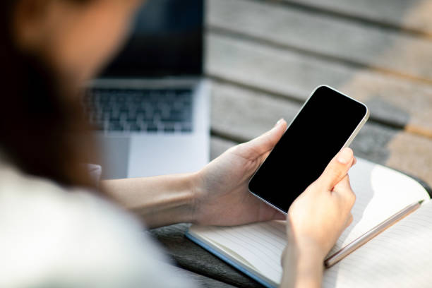 istock Close-up of a woman's hands holding a smartphone with a blank screen above an open notebook 2156284439