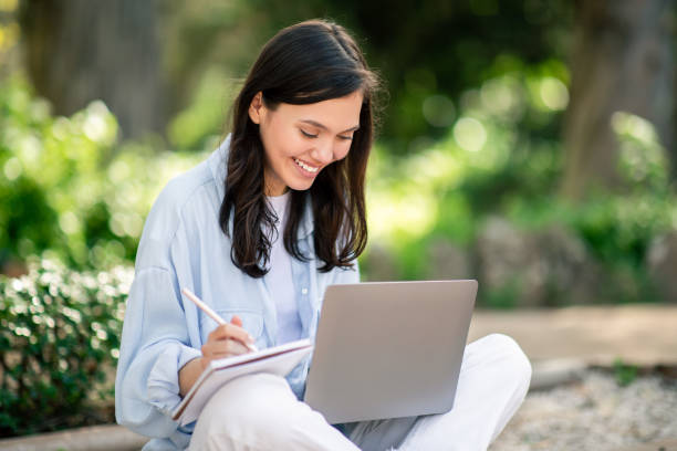 istock Focused young woman working on laptop in natural setting 2156284476