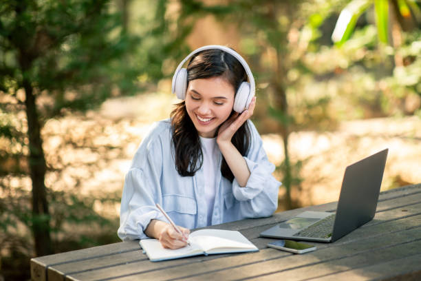 Woman writing in notebook with laptop and headphones