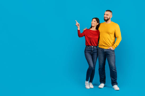 istock Joyful young couple standing side by side, woman pointing upwards with excitement 2156285432
