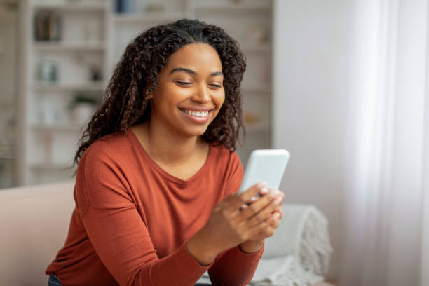 istock Black Woman Sitting on Couch Looking at Cell Phone 2156287669