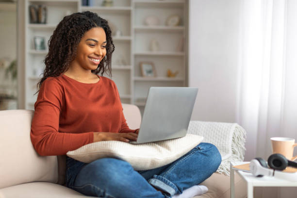 istock Happy Black Woman Sitting on Couch Using Laptop 2156287684