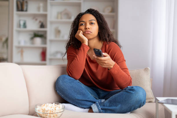 istock Black woman with remote controller looking bored while watching TV at home 2156287743