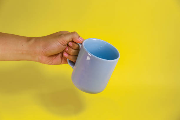 istock hand holding a blue ceramic mug on a yellow background 2156289861