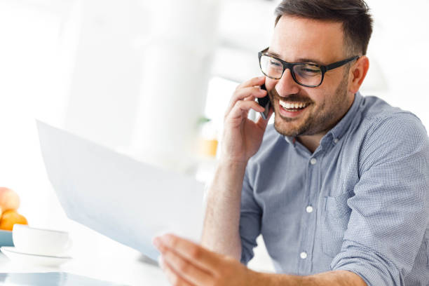 istock Happy businessman reading reports while talking on cell phone at home. 2156293882