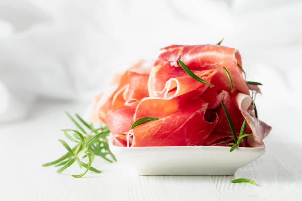 istock Prosciutto with rosemary on a white wooden table. 2156294327