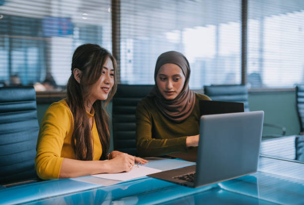 istock Two Asian businesswomen talking while working together with laptop in a modern office startup 2156295544