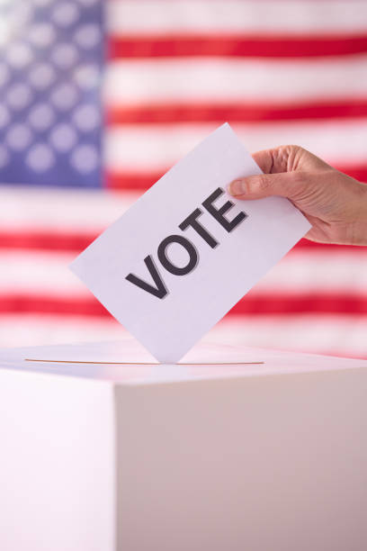 istock Hand Placing Vote In Ballot Box With American Flag Background 2156303599