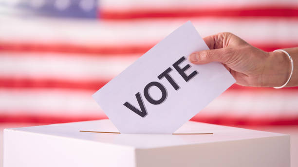 istock Hand Placing Vote Ballot Into Box With American Flag 2156303633