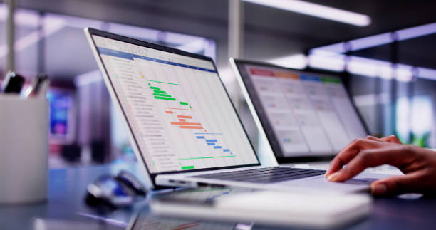 African American woman using laptop to manage multiple tasks and projects in a modern office setting African American woman using laptop to manage multiple tasks and projects in a modern office setting. Busy business professional. scrum stock pictures, royalty-free photos & images