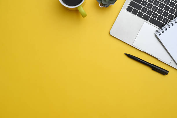 istock Laptop, notebook, pen and coffee cup on yellow background with copy space 2156308820
