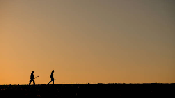 Two men farmers walk across the field, carrying work equipment. High quality photo