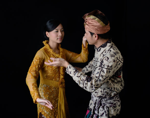 Indonesian man and woman in traditional attire performing a cultural dance against a dark background.