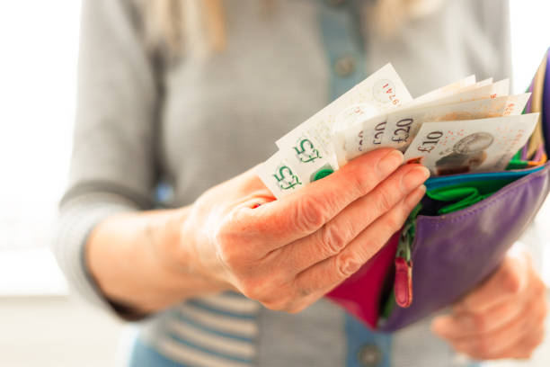 Senior woman taking bank notes from her wallet Close up color image depicting a senior woman in her 70s taking British bank notes from her colorful leather wallet. british currency stock pictures, royalty-free photos & images