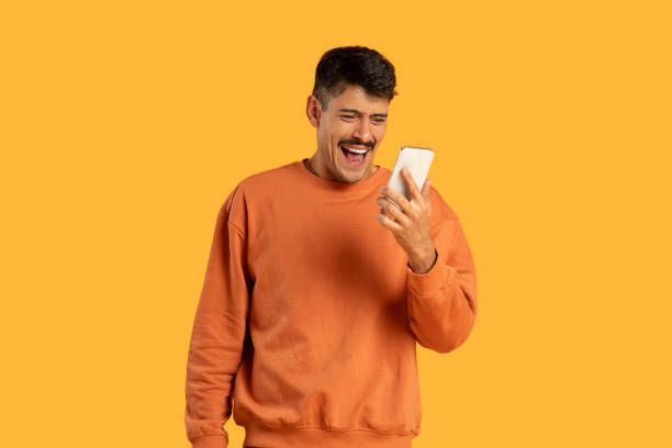 istock Man in Orange Sweater Holding Cell Phone And Exclaiming 2156329407