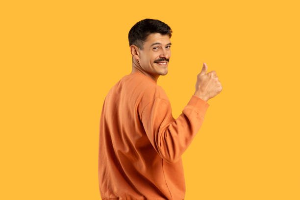 Smiling man giving thumbs up on yellow backdrop