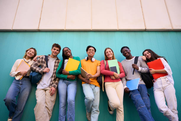 istock Low angle portrait of young multiracial students leaning against blue wall looking smiling at camera 2156331082