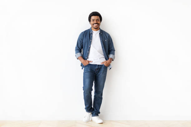 istock Cheerful black man standing confidently with hands in pockets against white wall 2156332323