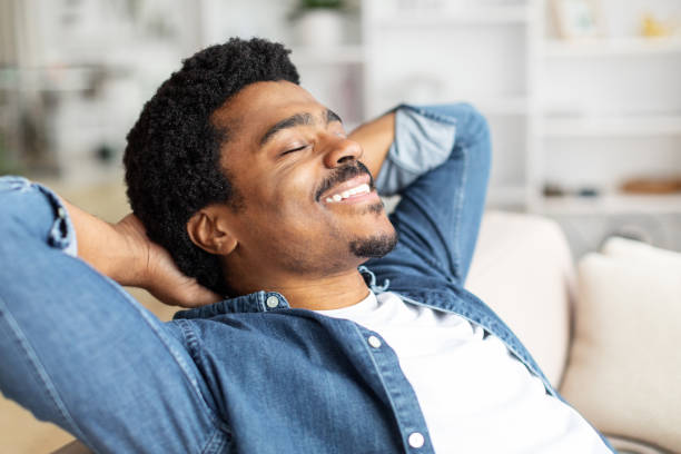 istock Black Man Relaxing on Couch With Hands Behind Head 2156332331