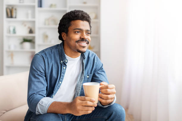 istock Man Sitting on Couch Holding Cup of Coffee 2156332503