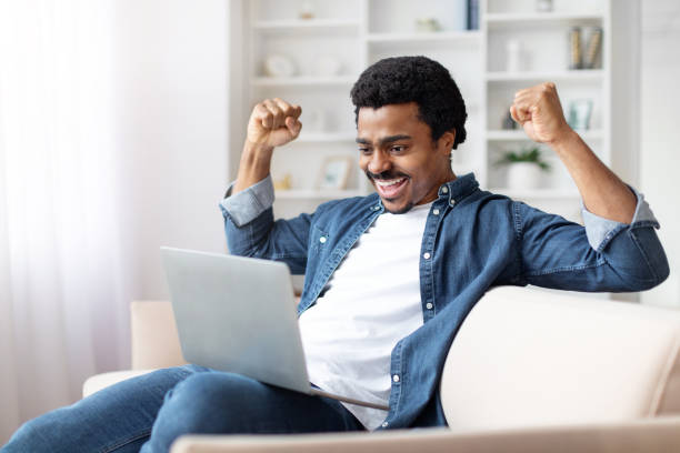 istock Excited Young Black Man Celebrating Success at Home With Laptop 2156332685