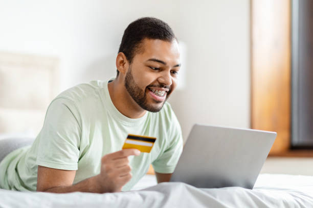 istock African american man with laptop and card on bed 2156334248
