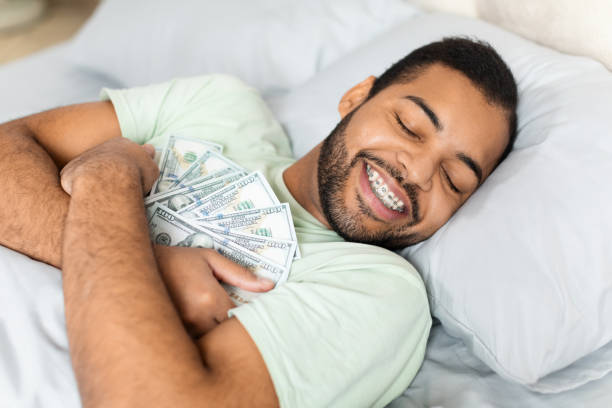 istock Man hugging cash in bed suggesting wealth 2156334289