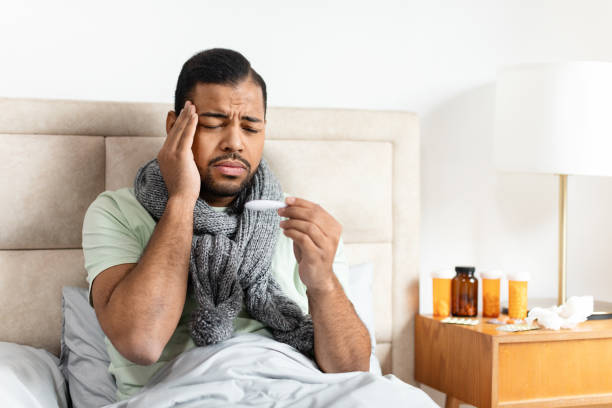 istock Man in bed with scarf checking thermometer 2156334296