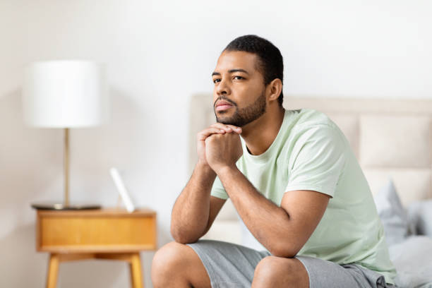 istock Thoughtful Young Man Sitting on Bed in Bedroom During Daytime 2156334451