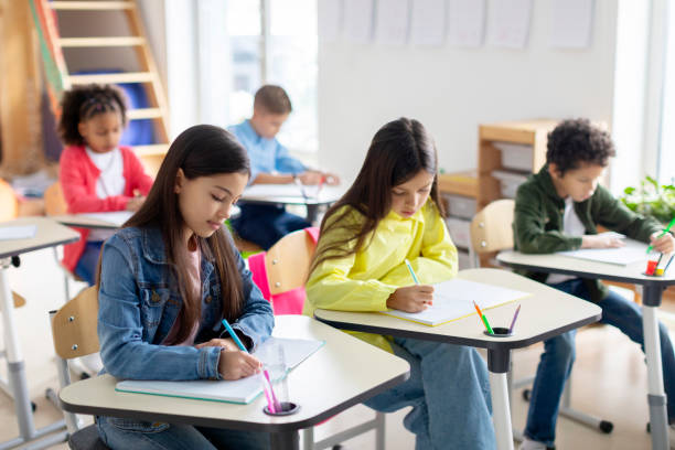 istock Engaged pupils children sitting at desks, writing in copybooks, having test, creating studious atmosphere in classroom interior in school 2156339647