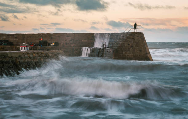 Waves hitting the stone wall in Cove Harbour, Scotland, with evening light and a man standing on the sea wall. Long Exposure