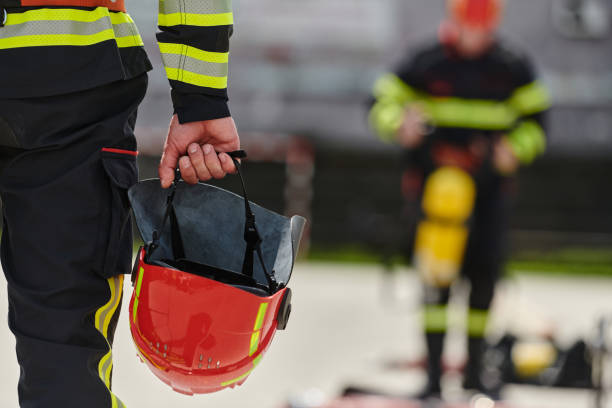nahaufnahme der hand eines feuerwehrmanns, der den feuerwehrhelm hält - feuerwehrmann stock-fotos und bilder