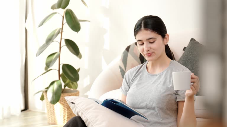 Middle age woman sit on sofa reading textbook increasing knowledge. Divergence.