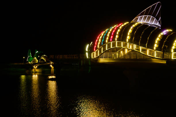 Uljin, South Korea - May 18th, 2024: Night view of the illuminated Uljin Sweet Fish Bridge featuring LED-lit fish sculptures reflecting on Namdae Stream's waters, highlighting the vibrant colors and architectural beauty.