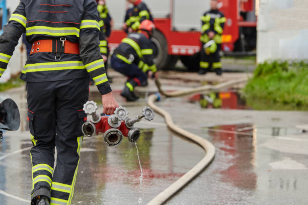 In a dynamic display of synchronized teamwork, firefighters hustle to carry, connect, and deploy firefighting hoses with precision, showcasing their intensive training and readiness for challenging and high-risk situations ahead stock photo