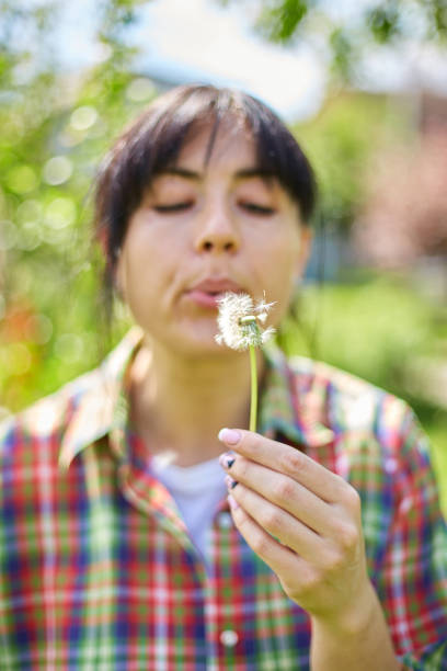 istock Woman Blowing Dandelion Seeds in a Sunny Garden During Springtime 2156357714