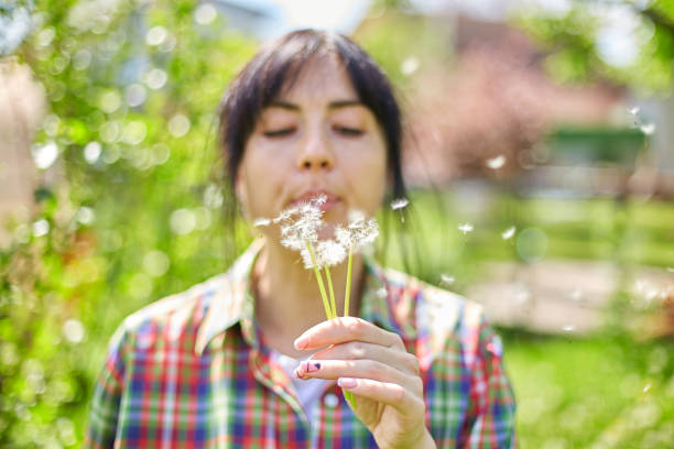 Beautiful hispanic woman blowing dandelion seed in green meadow, close up side view