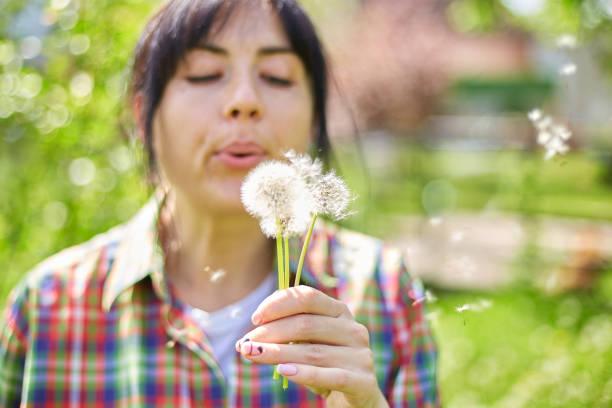 istock Woman Blowing Dandelion Seeds in a Sunny Garden During Springtime 2156357732