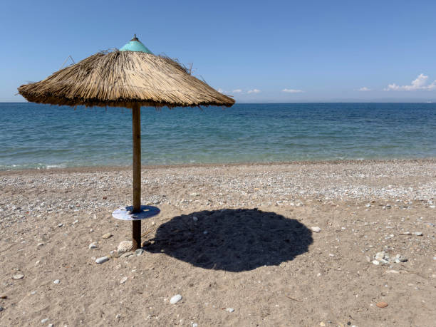 Straw beach rattan parasol at empty beach with beautiful calm sea or ocean coast under blue sky. Relaxing summer day. Idyllic travel and summer vacation concept. Straw umbrella on beach