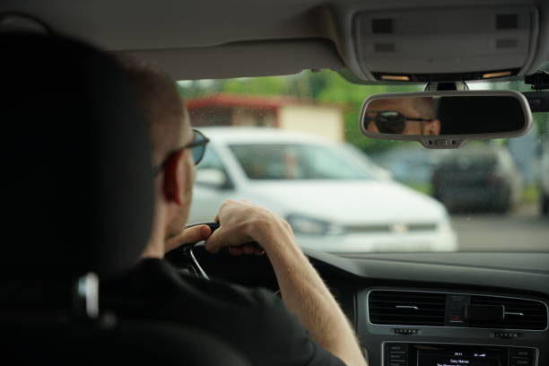 istock A man is seen from the back while driving a car, wearing sunglasses and looking through the windshield with a white car visible in front. 2156362754