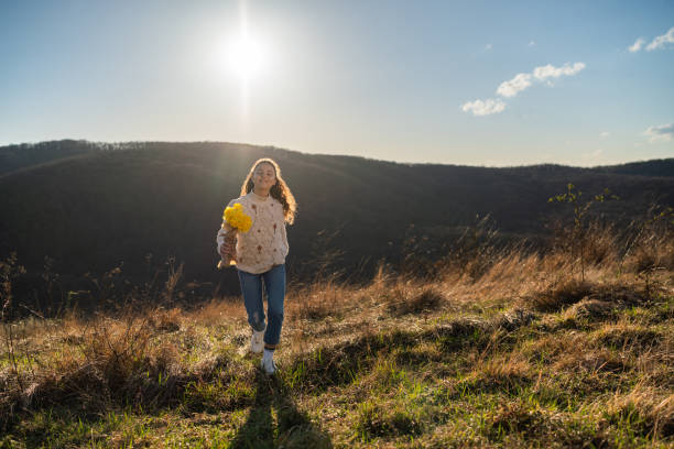 Full length of a happy teenage girl whit flowers walking on a mountain at sunset