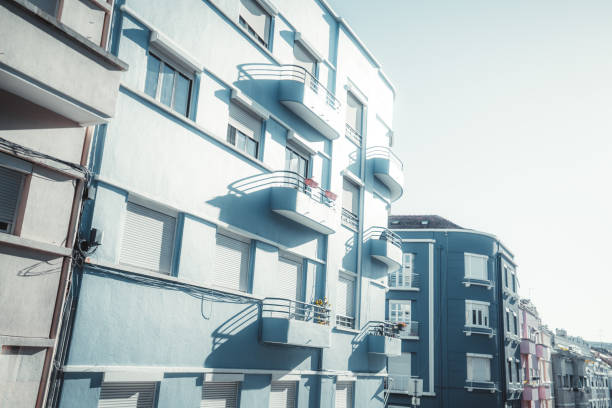 A typical street in Lisbon, featuring pastel-colored residential buildings with multiple balconies. The architectural style showcases clean lines and a uniform color palette; shadows cast by the sun