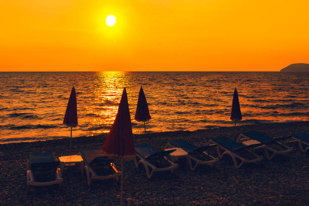 Beach chairs and umbrellas on pebble shore at sunset.
