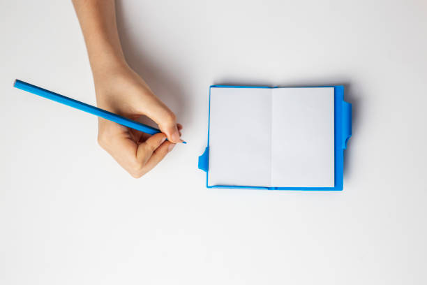 hand holding blue pencil and writing in notebook on white background isolated copy space