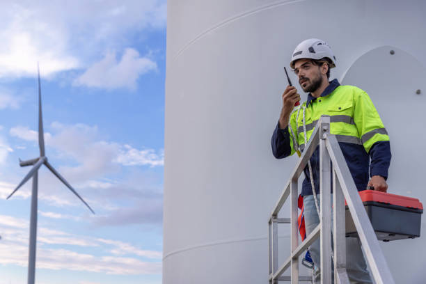 istock Professional Man Maintenance engineers working in wind turbine farm at sunset.  Engineer Man standing among Wind Energy Turbine. 2156380796