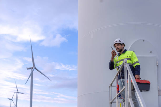 istock Professional Man Maintenance engineers working in wind turbine farm at sunset.  Engineer Man standing among Wind Energy Turbine. 2156380797
